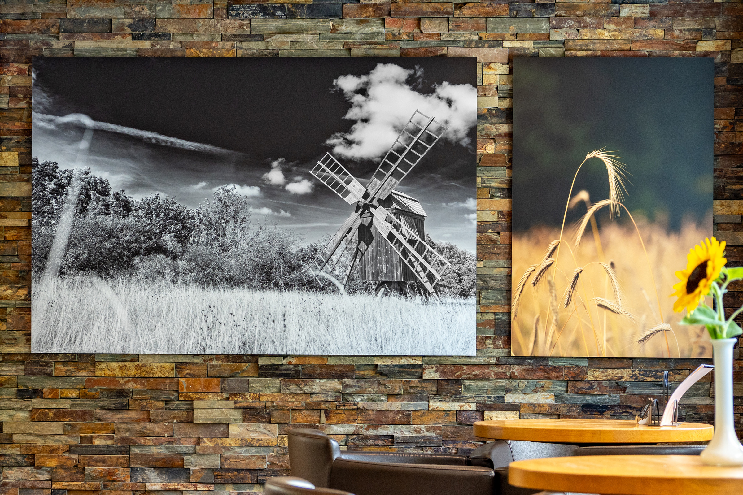 Zwei Kunstdrucke an einer Steinwand: Schwarz-weisse Windmühle und farbige Weizenfeldfotografie