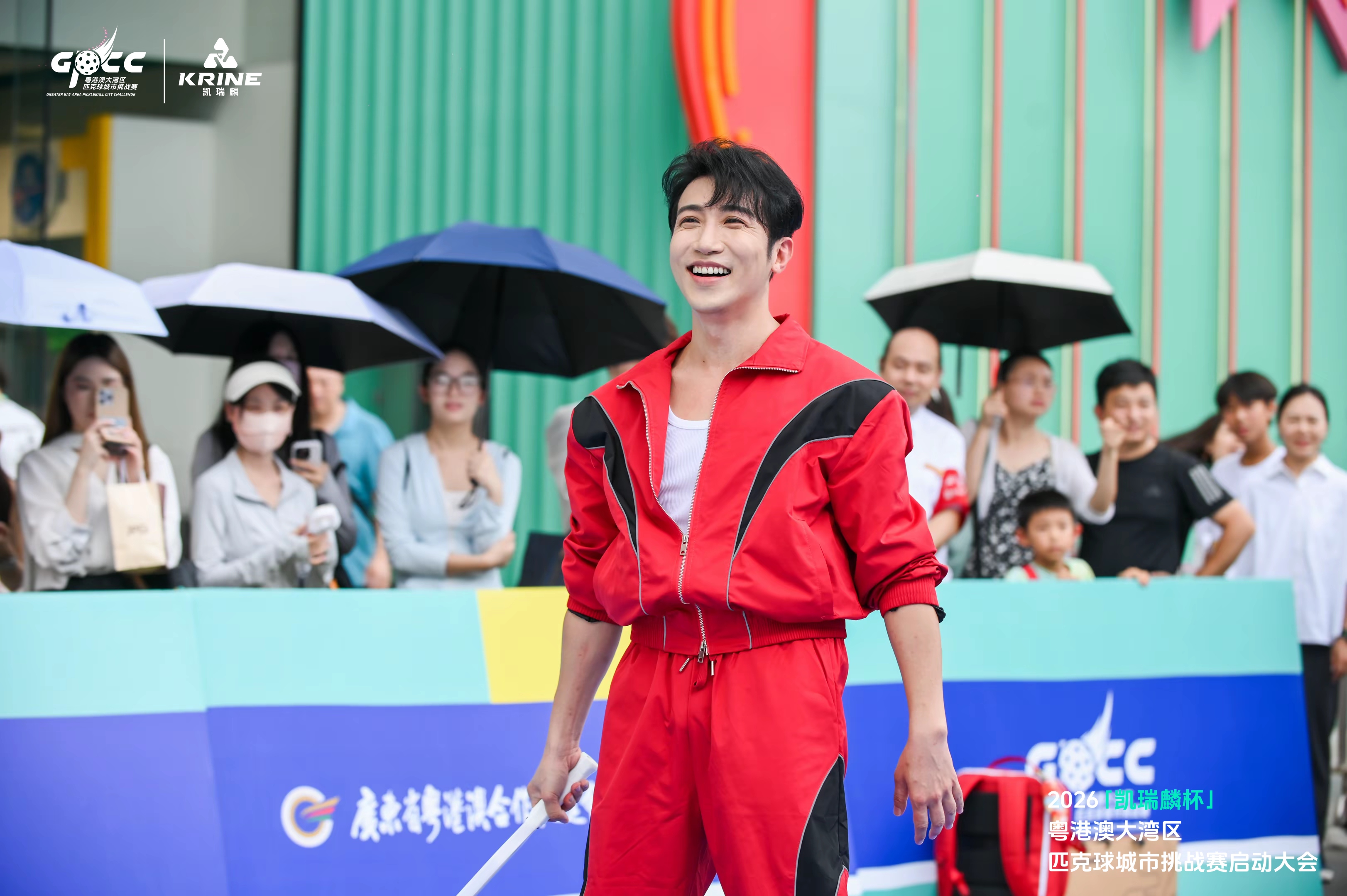 Guest in a red tracksuit holding a paddle among the crowd