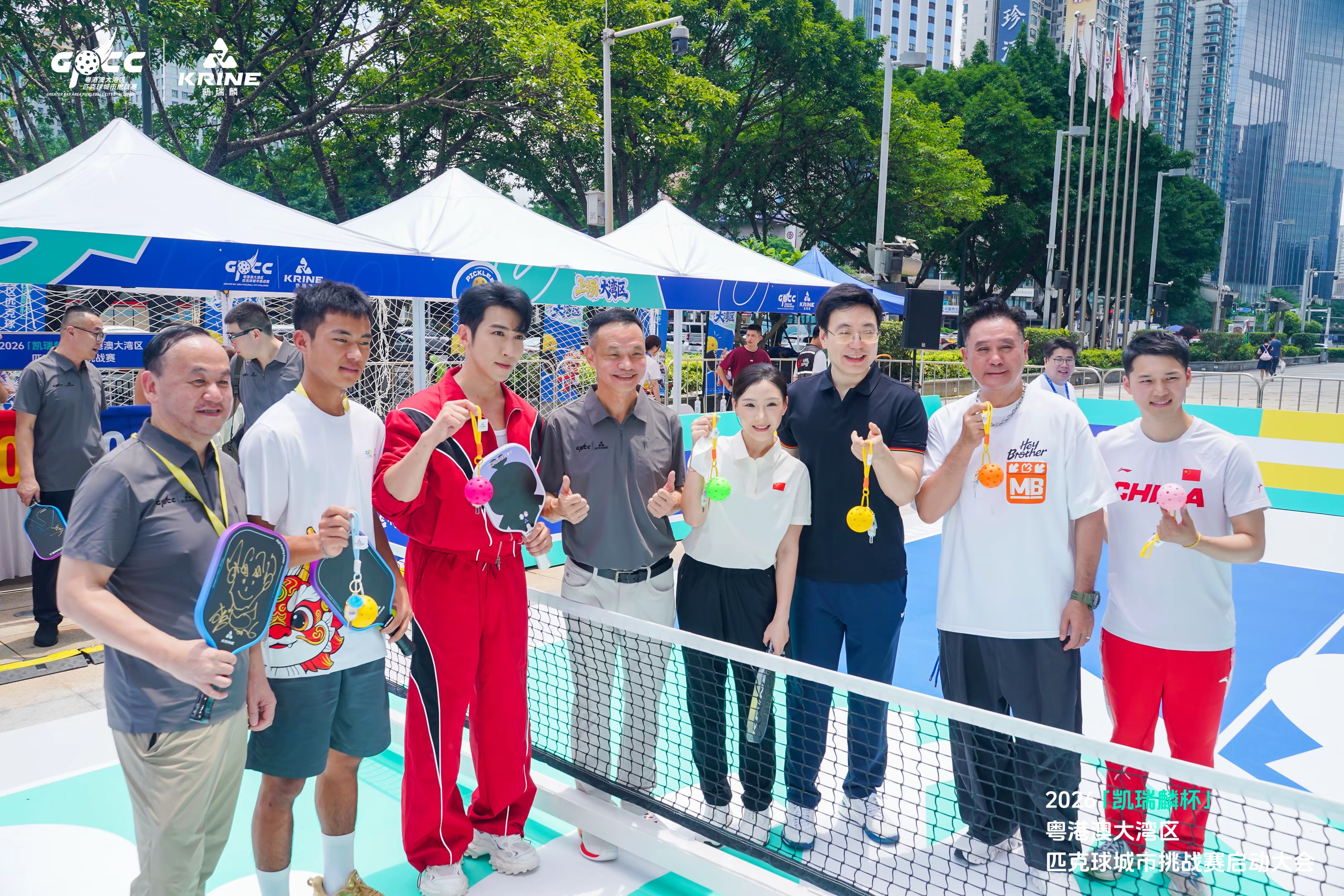 Group of eight posing behind the pickleball net with paddles