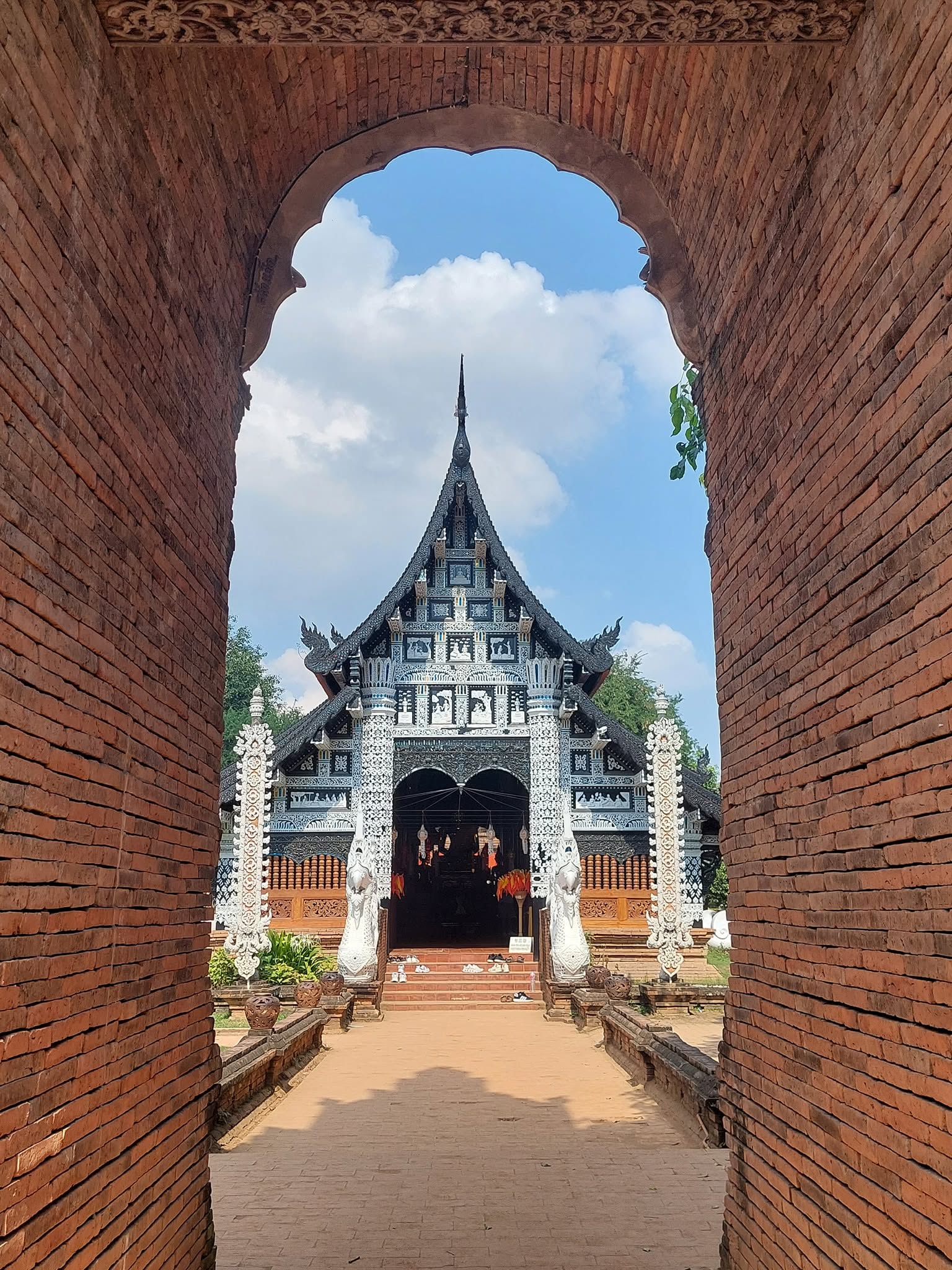 Ornate Thai temple viewed through a weathered brick archway with blue sky