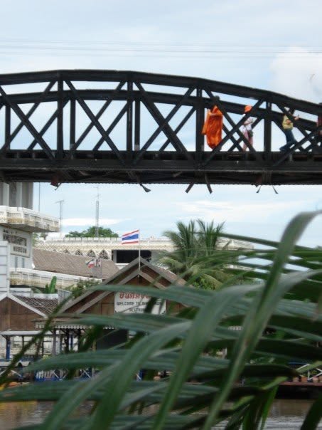 Historic steel truss bridge over the River Kwai with people walking across including a monk