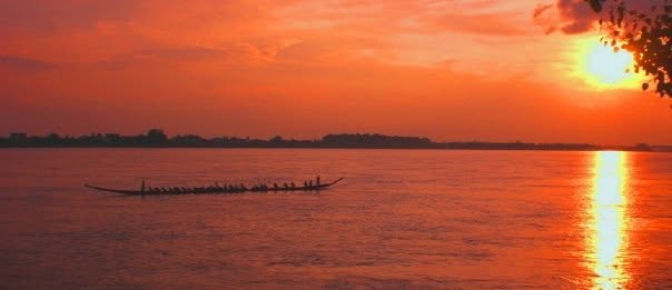 Traditional wooden boat on a calm river at sunset with vibrant orange sky
