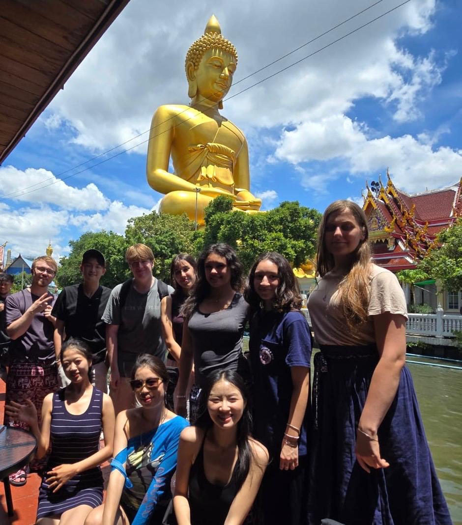 Group of ten people on a boat posing with the giant golden Buddha statue in the background