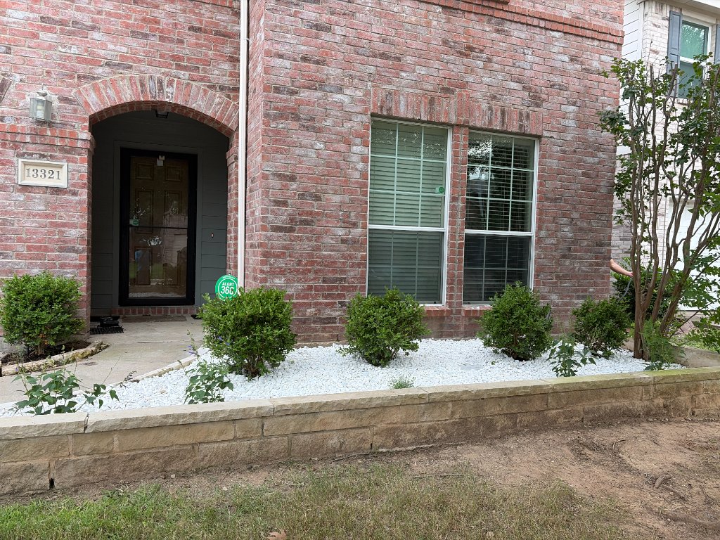 Stacked stone retaining wall with a white rock bed and trimmed shrubs