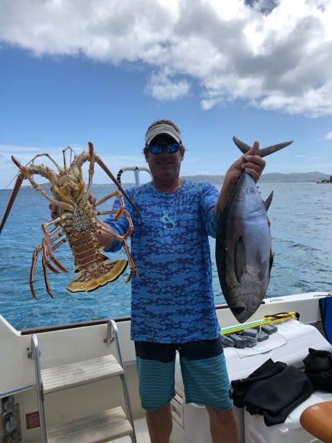 Gregory P. Smith on the water in the Virgin Islands, holding a spiny lobster and a fish