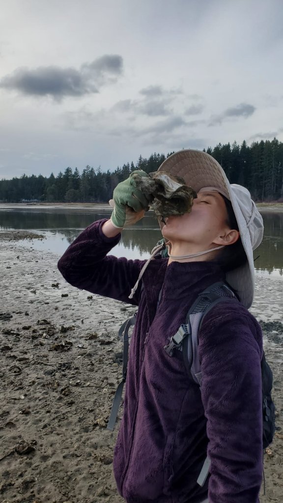 Maya shucking an oyster on the shoreline
