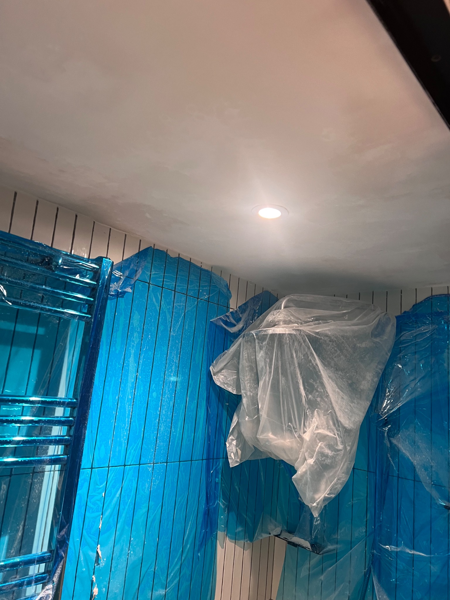 Bathroom ceiling mid-restoration, protected with blue sheeting while loose paint is removed and the surface is prepared