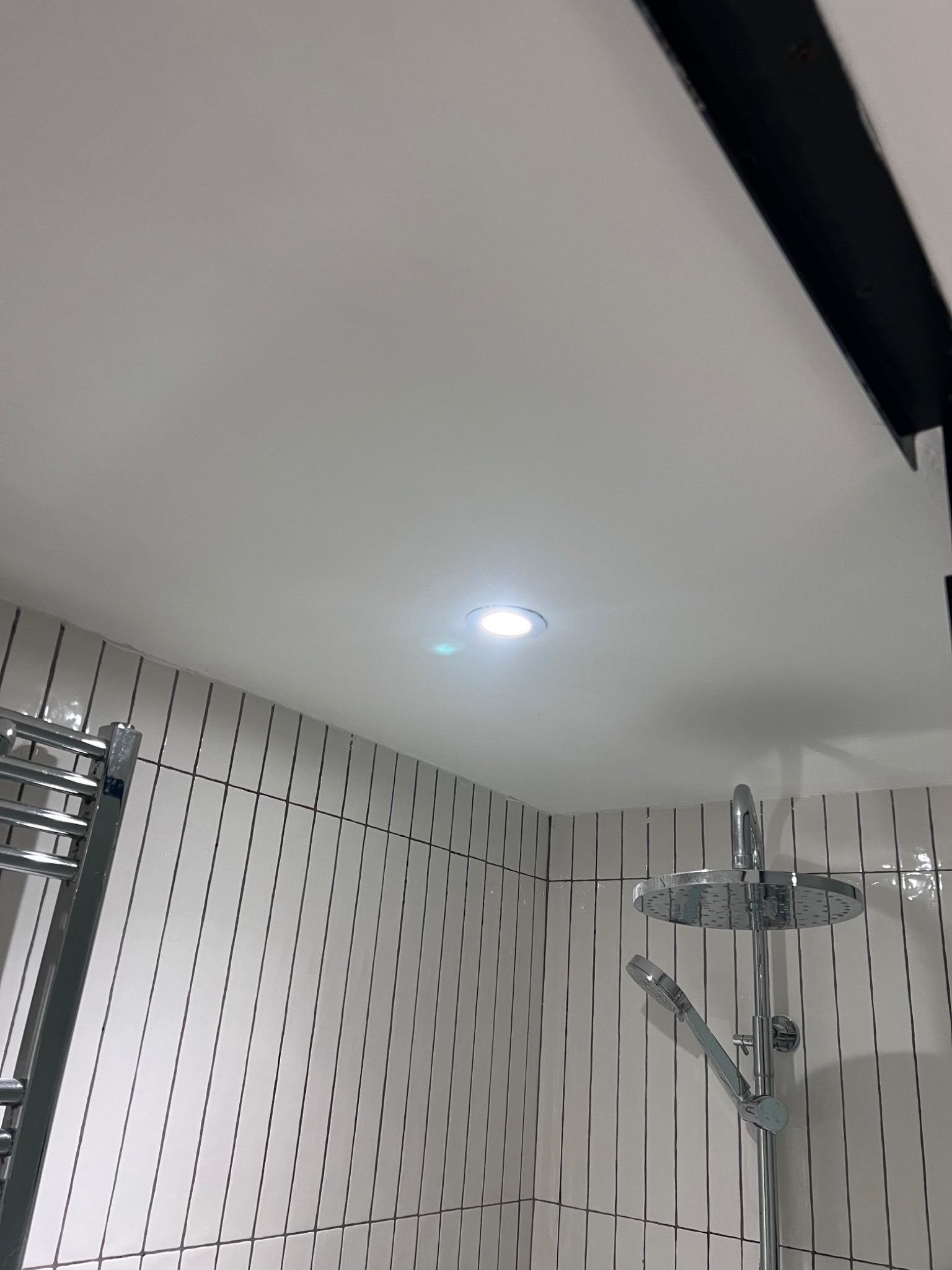 Pristine white finished bathroom ceiling with a single glowing recessed downlight meeting a cleanly tiled wall — a 5-star hotel-standard finish