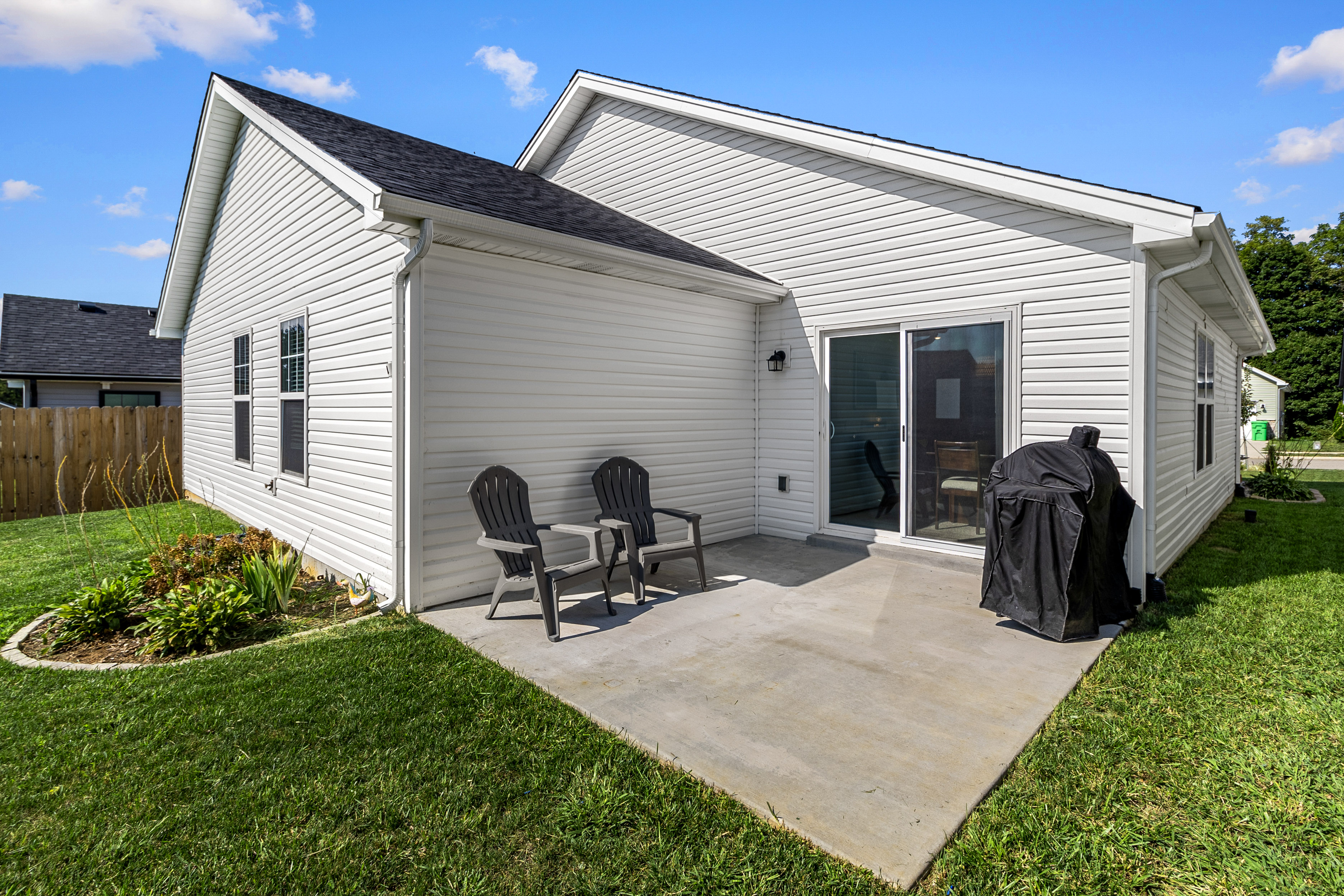 Rear patio of a white-sided home with chairs and grill overlooking the yard