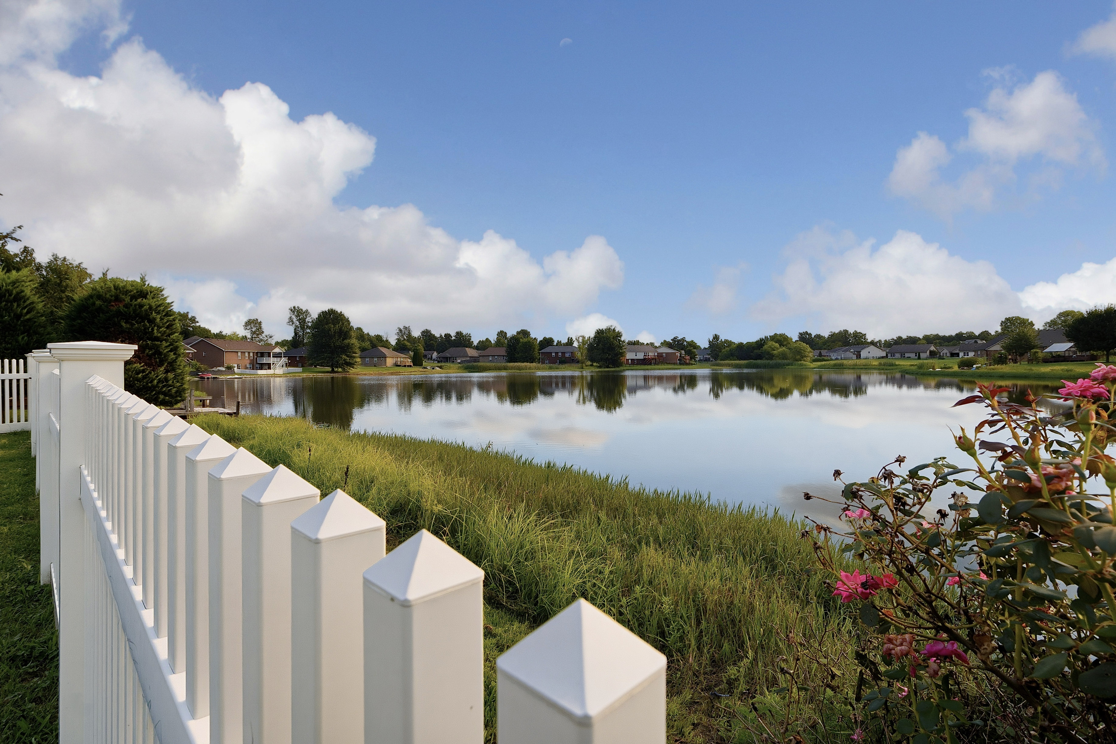 Serene neighborhood pond with white picket fence and reflections