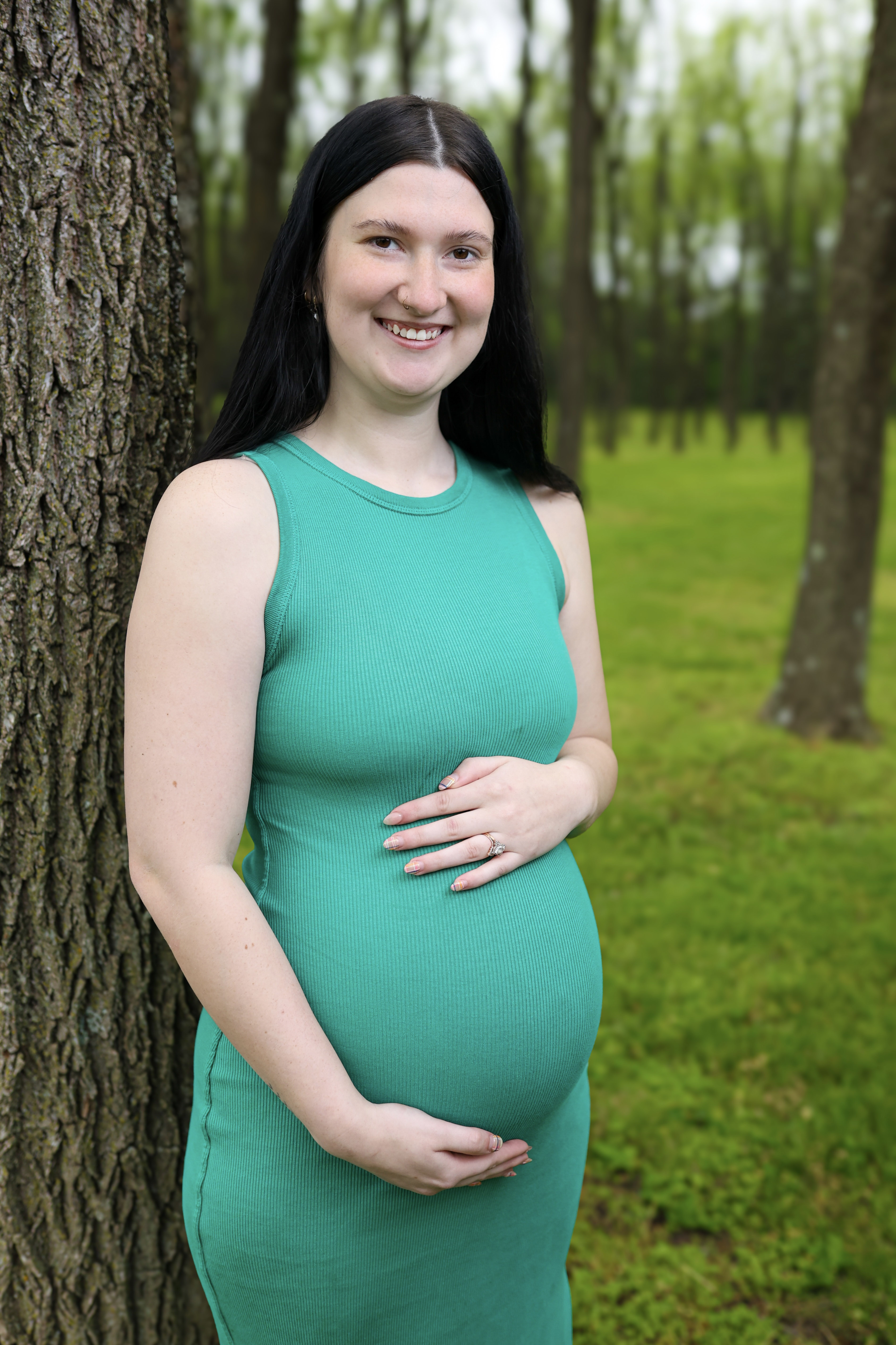 Maternity portrait in an emerald green dress beside a tree trunk