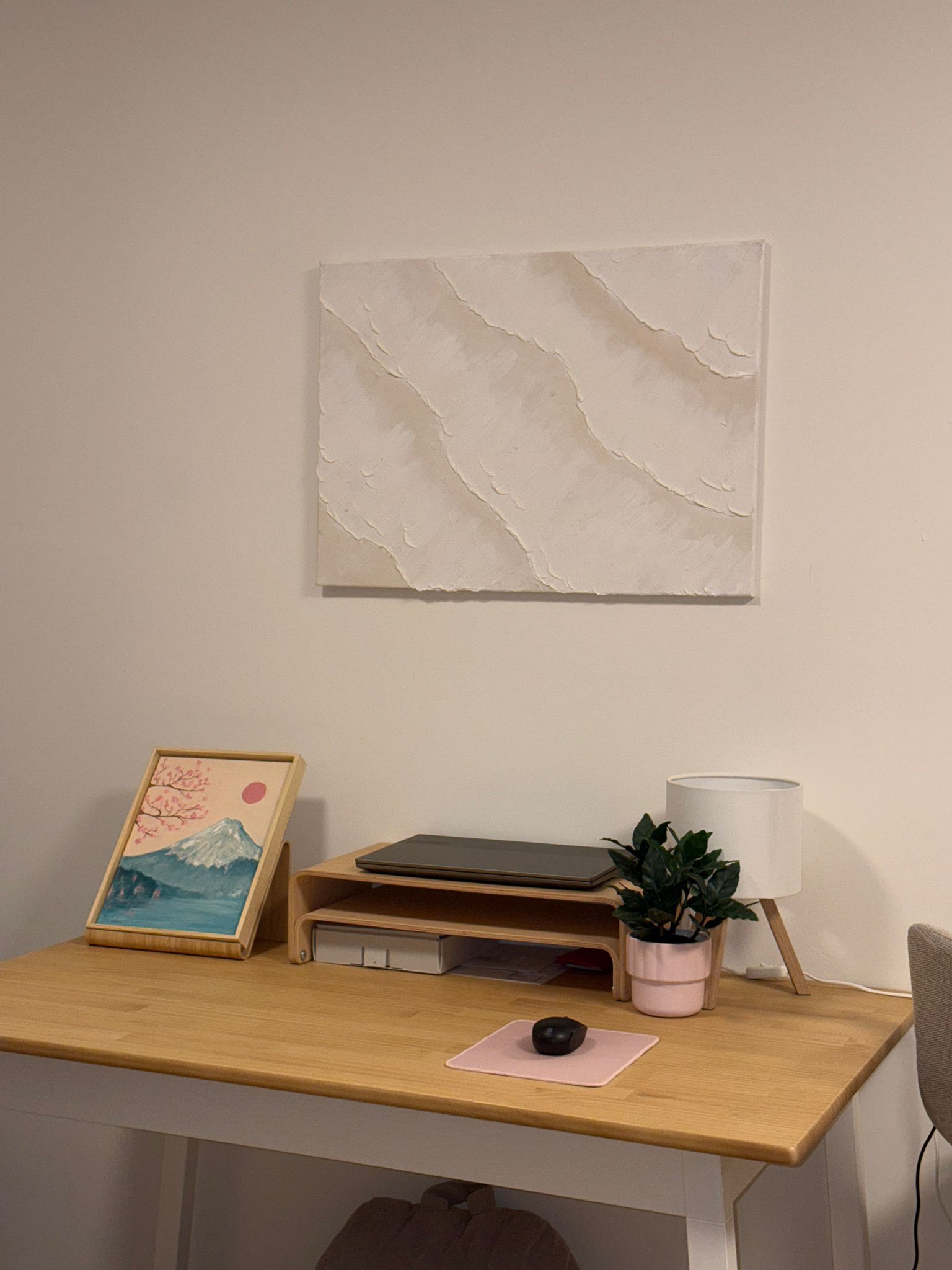 Textured white acrylic painting hanging above a wooden desk with plants and lamp in a cosy home office