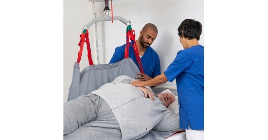 Caregivers using a ceiling-mounted hoist and transfer sling to reposition a bariatric patient