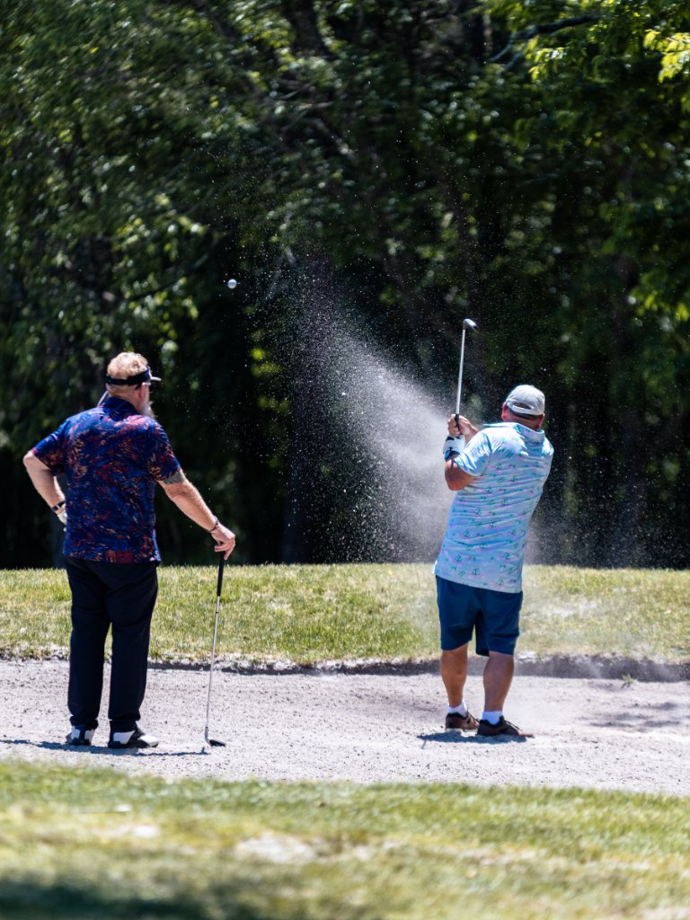 Golfer blasting out of a bunker with sand and water splashing