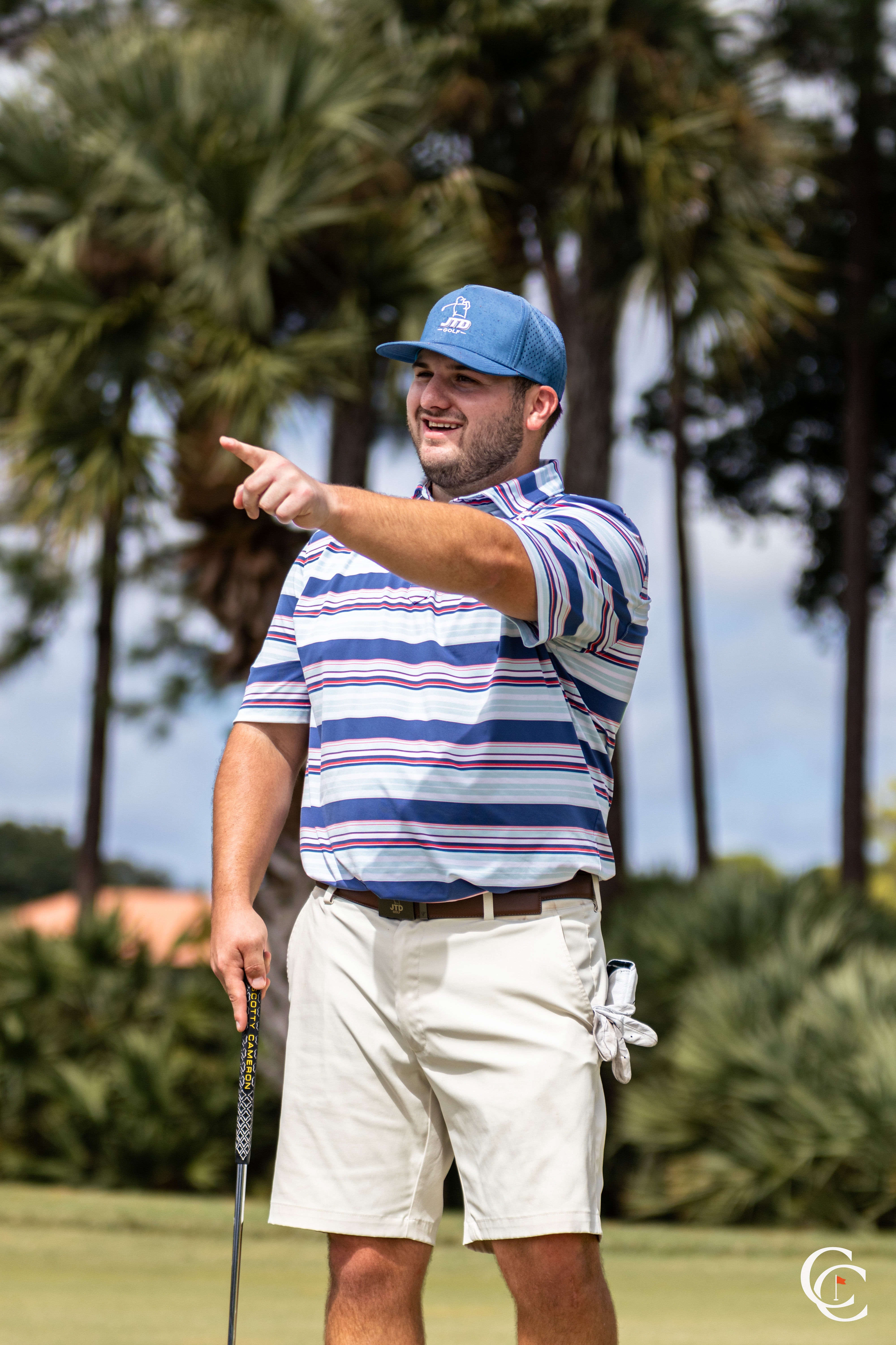 Golfer in striped polo smiling and pointing with his putter