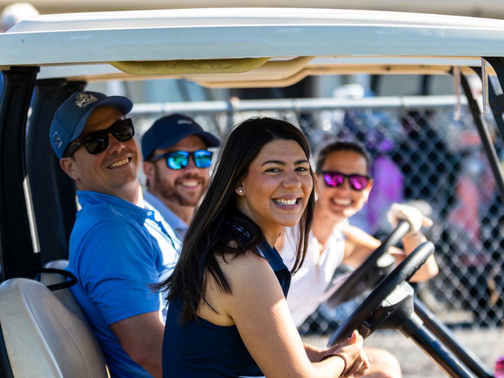 Four golfers laughing together in a golf cart