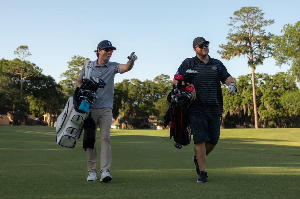 Two golfers carrying bags and walking the fairway
