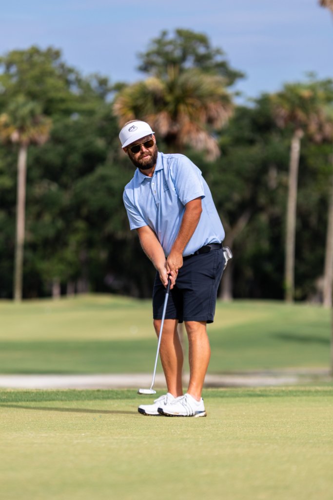Golfer putting on a sunny green with palm trees in the background