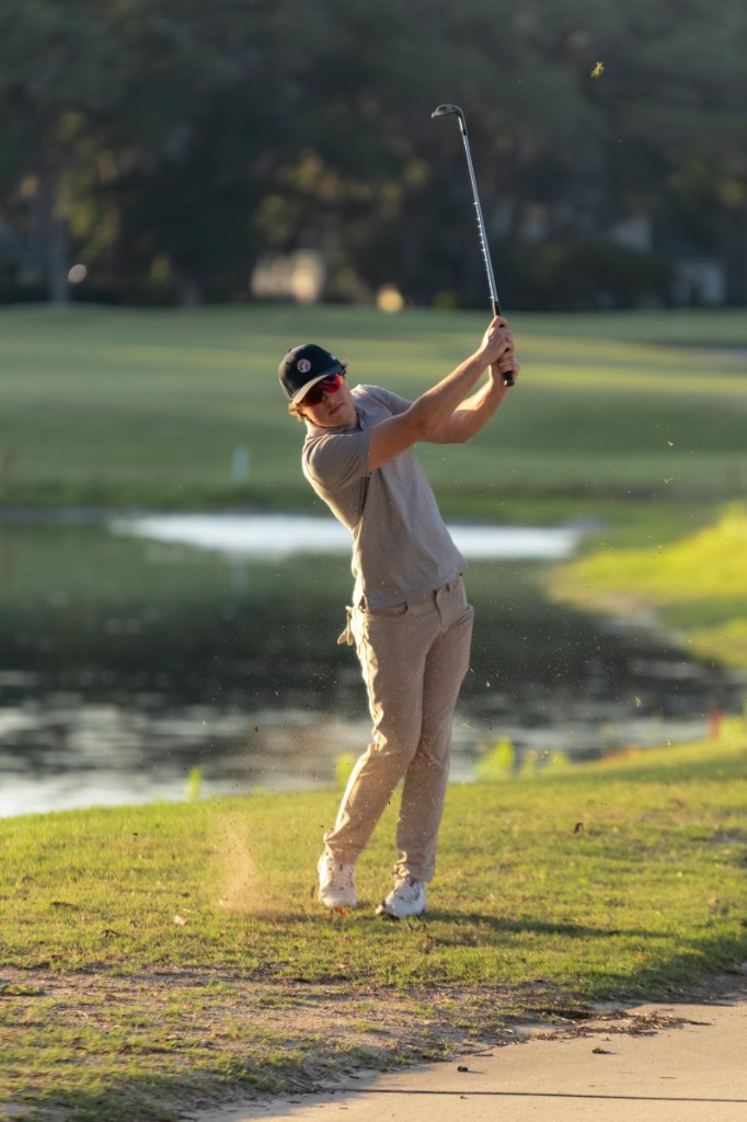 Golfer hitting an iron in late afternoon light with turf flying
