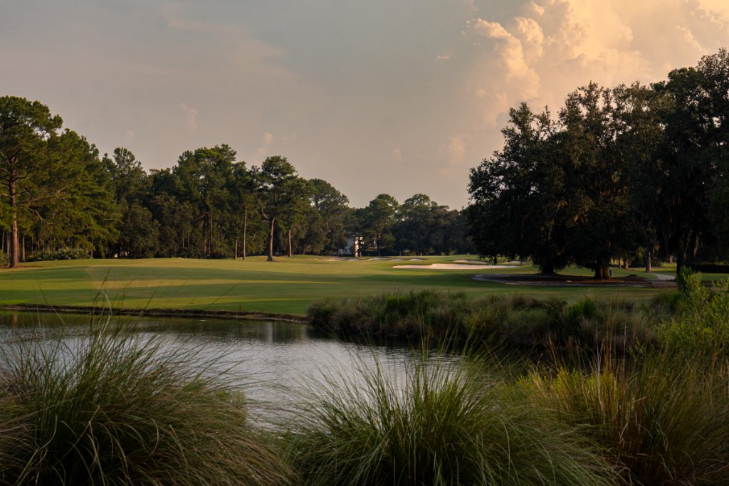 Lush fairway and green with pond and Spanish moss trees under dramatic clouds