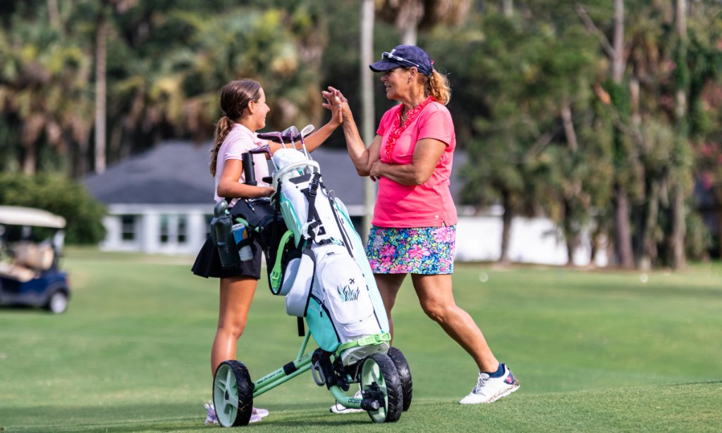 Young girl and woman high-fiving on the fairway with push carts