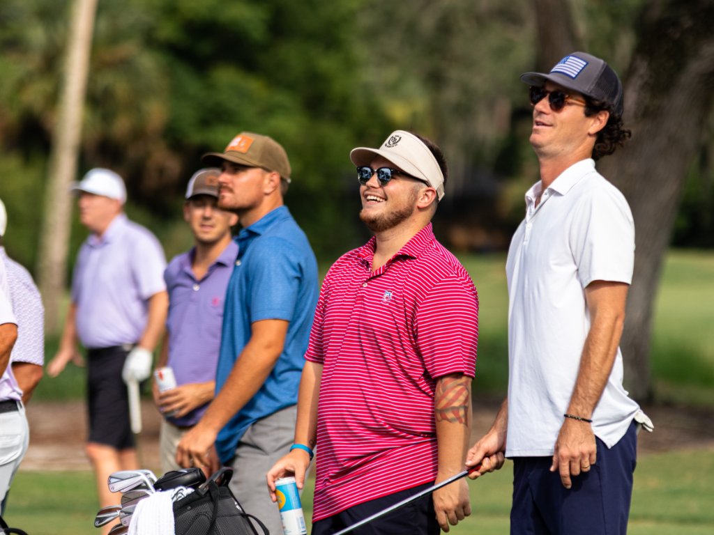 Golfer with tattoos giving a thumbs up walking with his group and bags