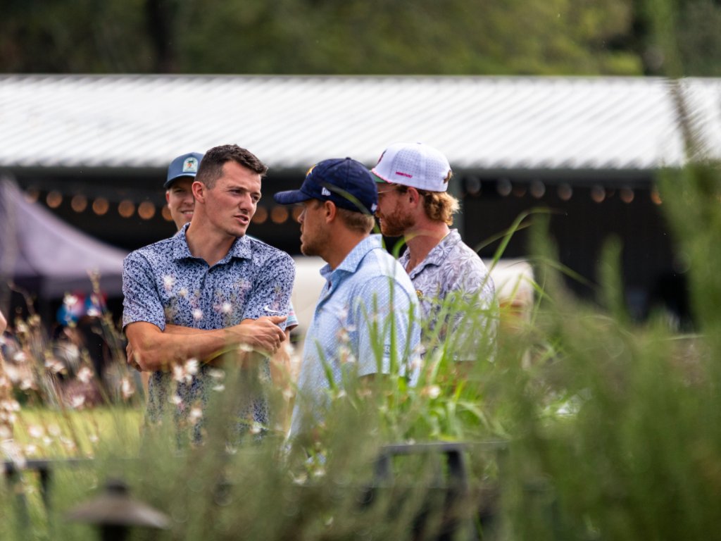 Three golfers chatting in the rough framed through tall grass
