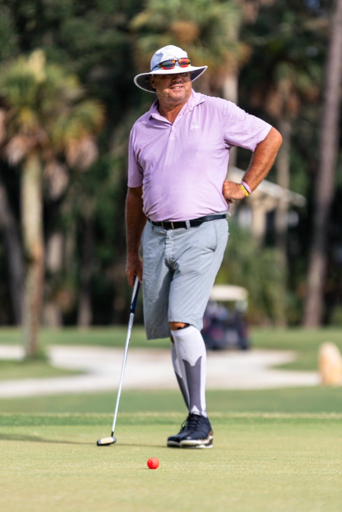 Golfer in lavender polo and sun hat smiling after a putt on the green