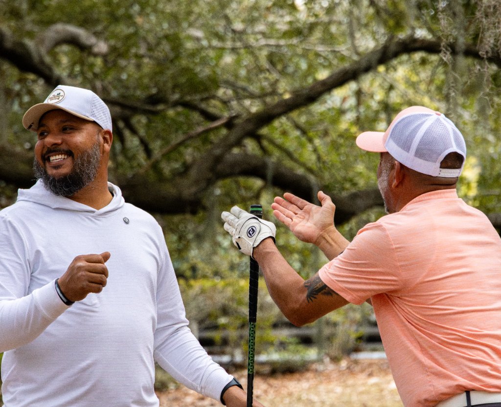 Two golfers laughing and high-fiving under a large tree