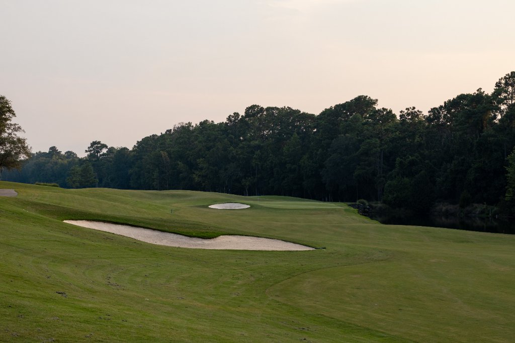 Wide fairway with bunkers and tree line at dawn light