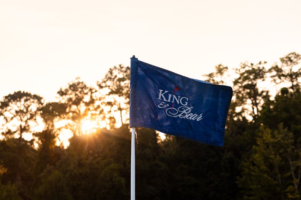 King & Bear flag waving at sunset with golden light through the trees