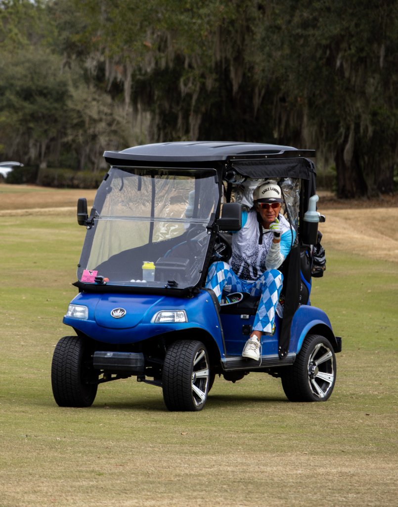 Colorful golfer in blue argyle cart pointing finger guns
