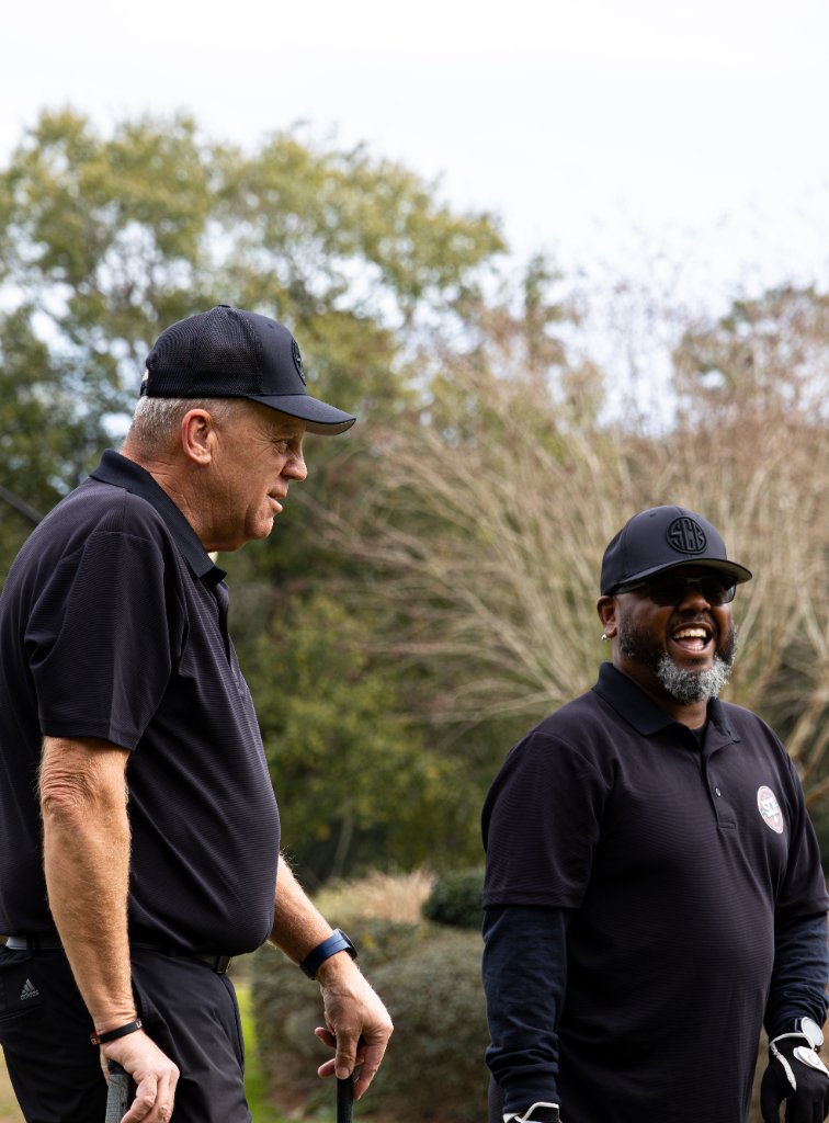 Two men in matching black outfits laughing on the course