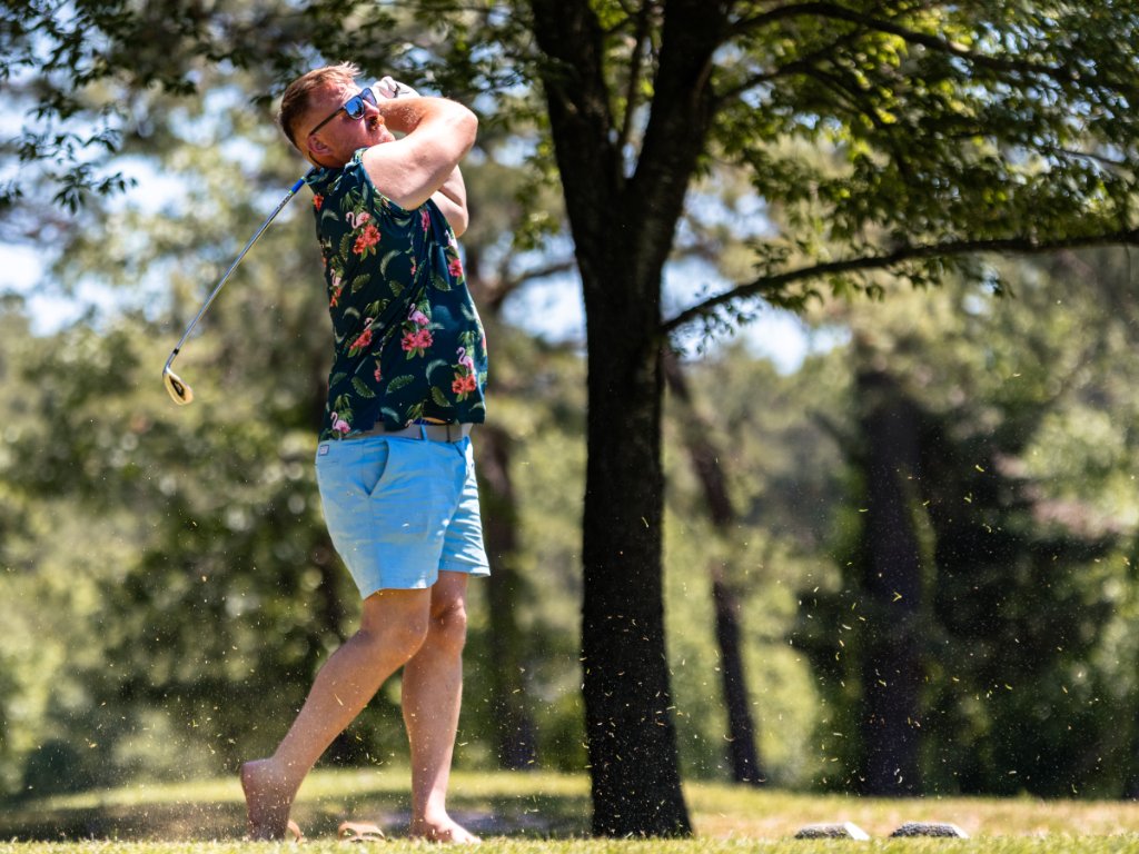 Golfer in flamingo-print shirt mid-swing with turf flying
