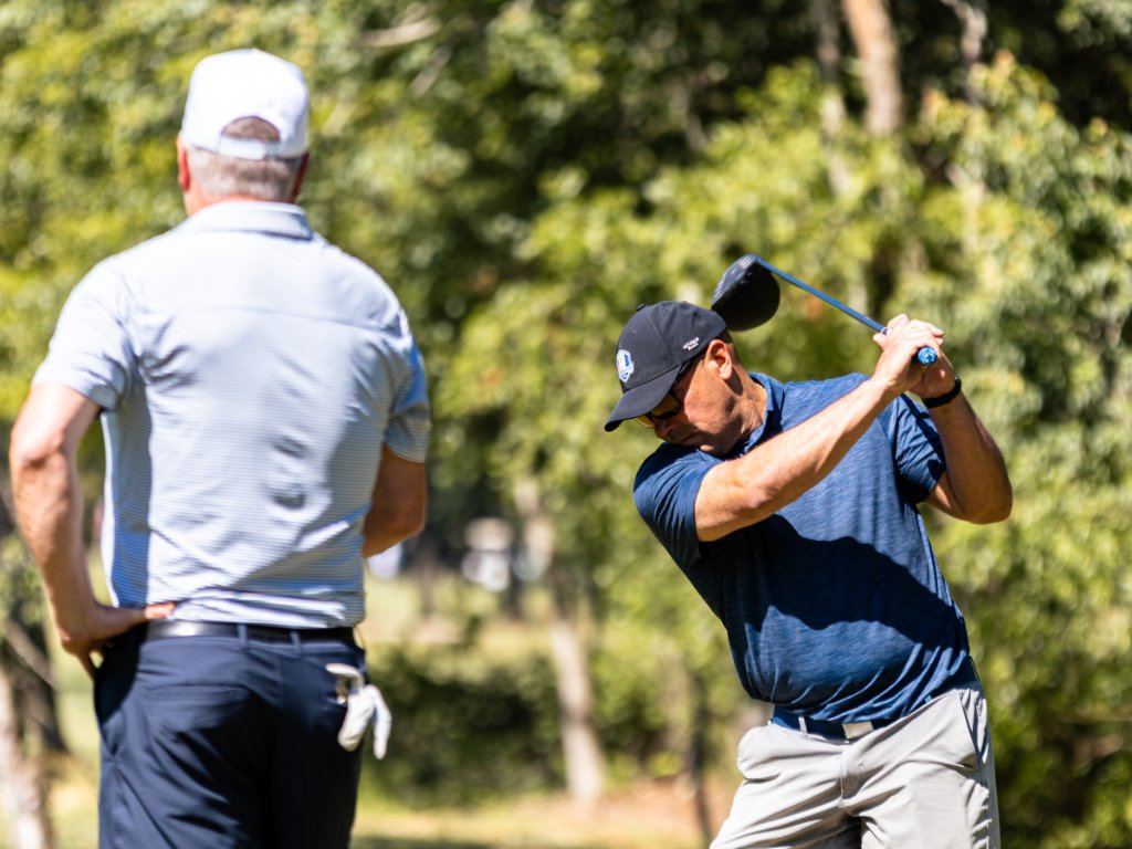 Golfer mid-swing with driver while partner watches from behind