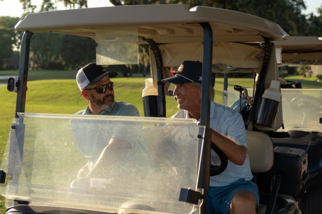 Two golfers riding in a cart at golden hour