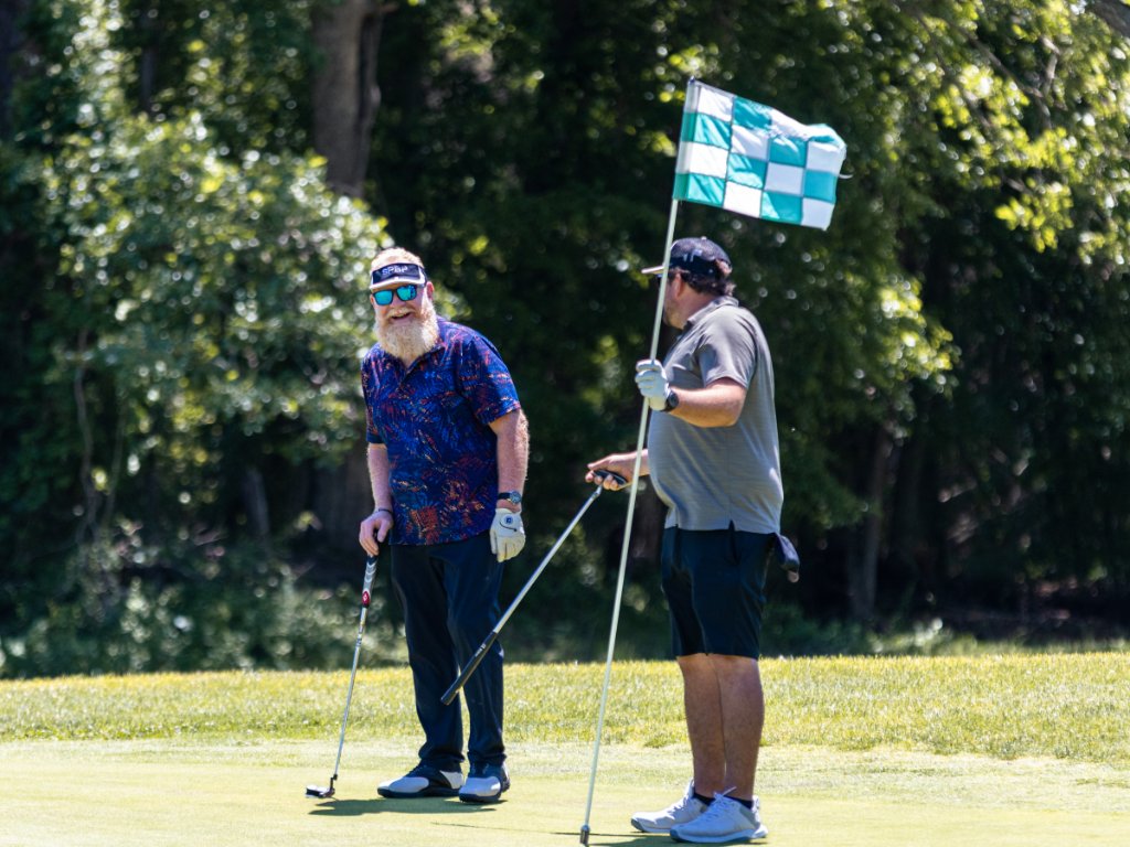 Two men on the green, one holding the flagstick