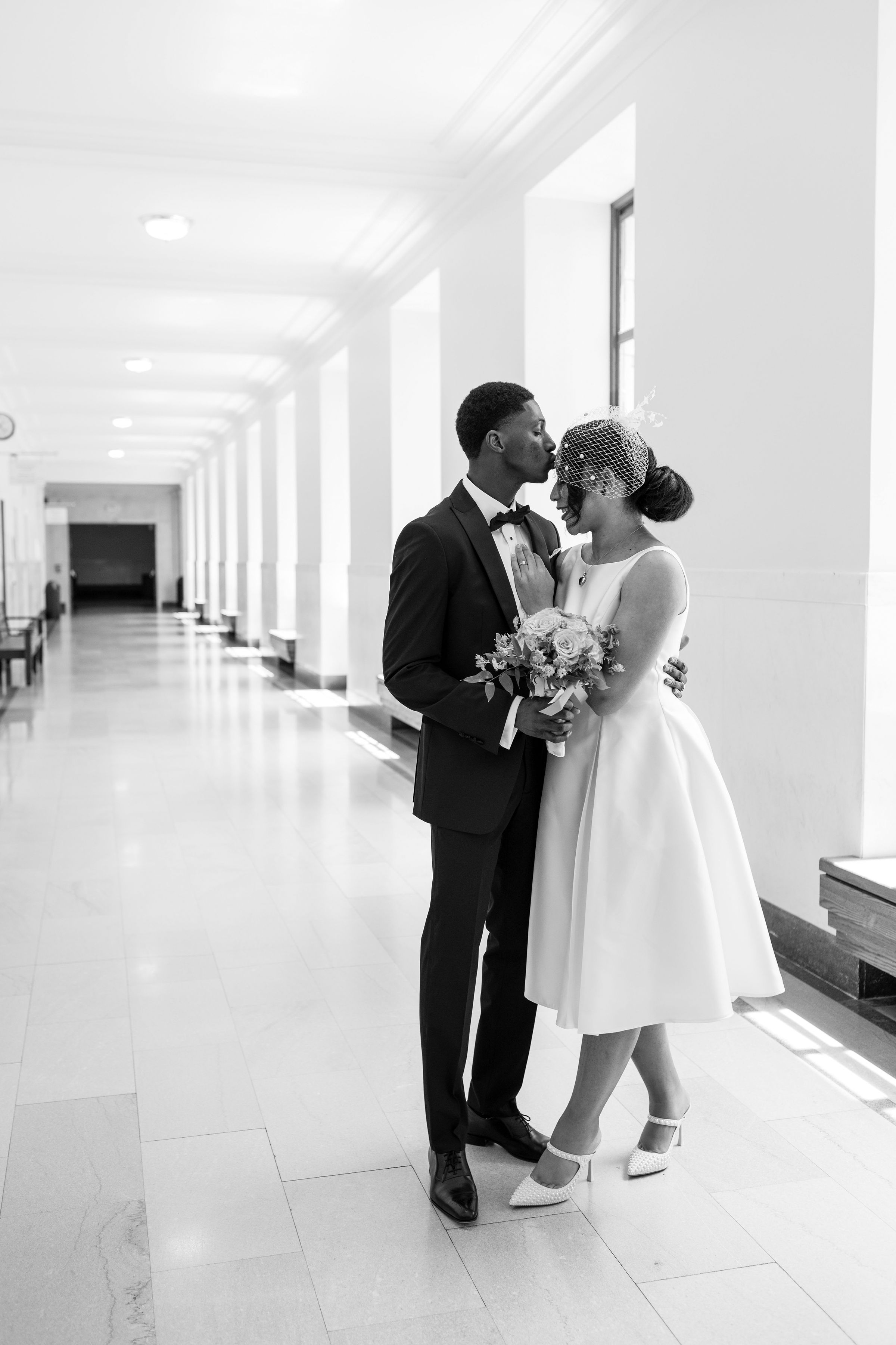 Groom kissing bride on the forehead in a bright corridor