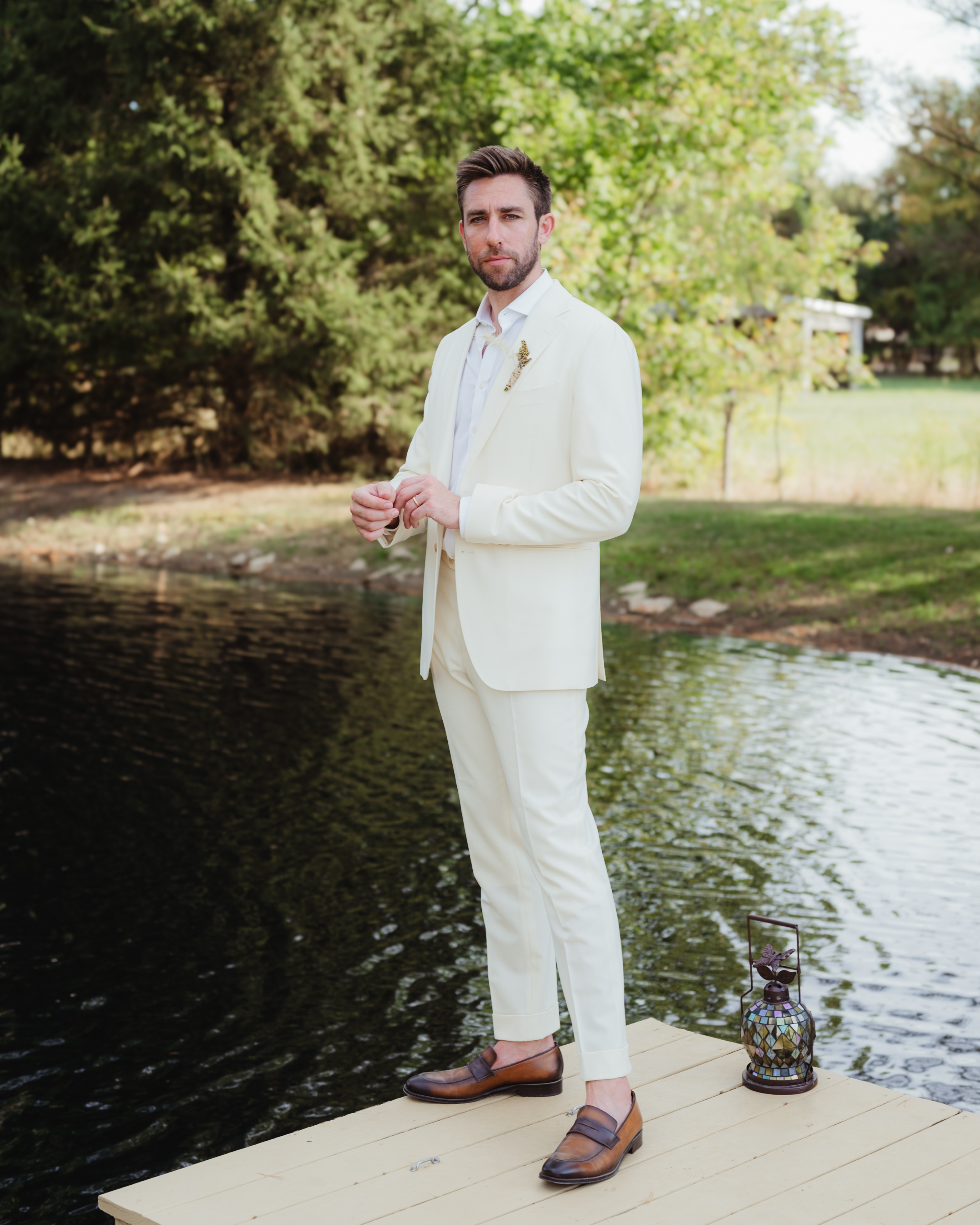 Groom standing on a wooden dock by a pond