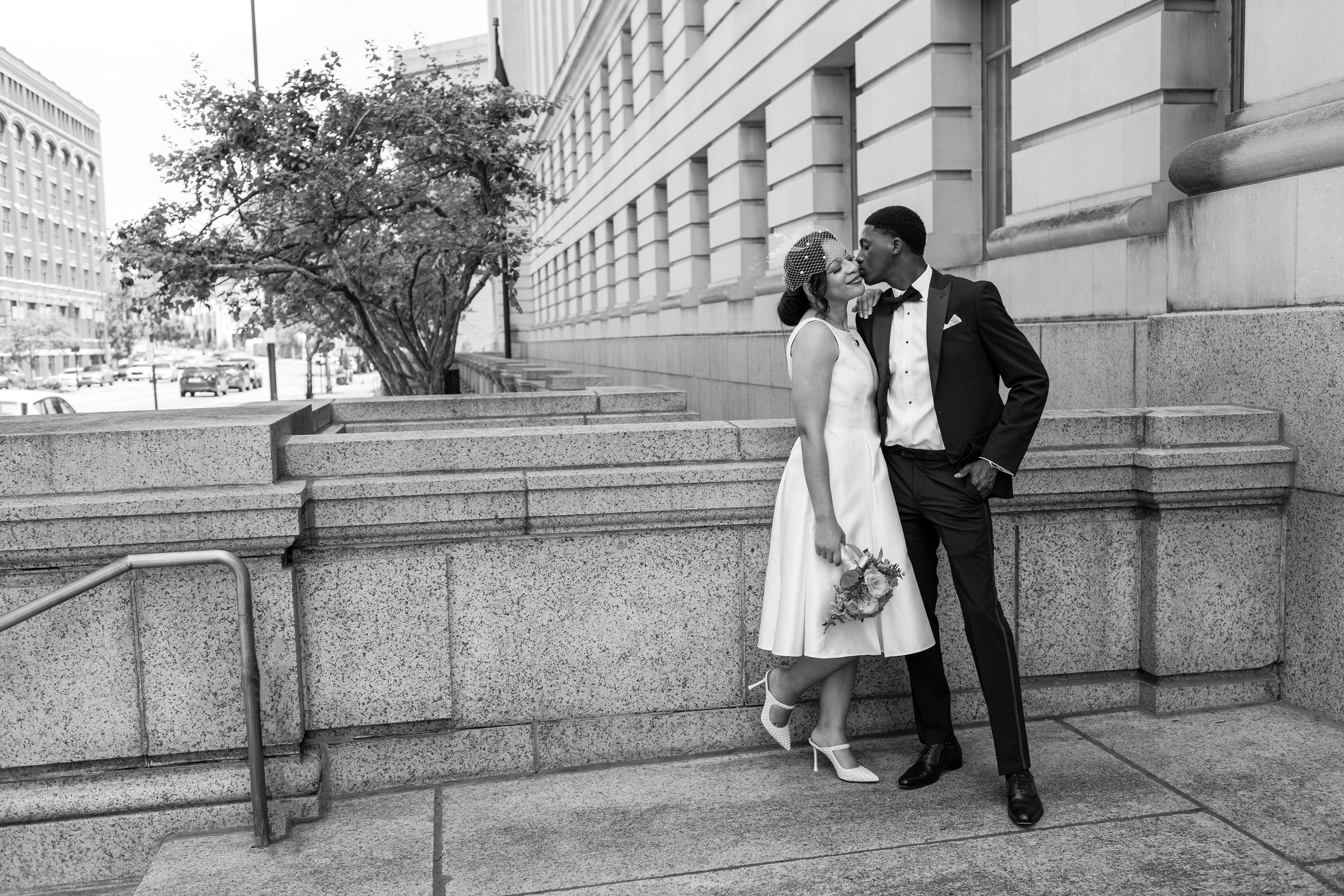 Groom kissing bride beside a stone building