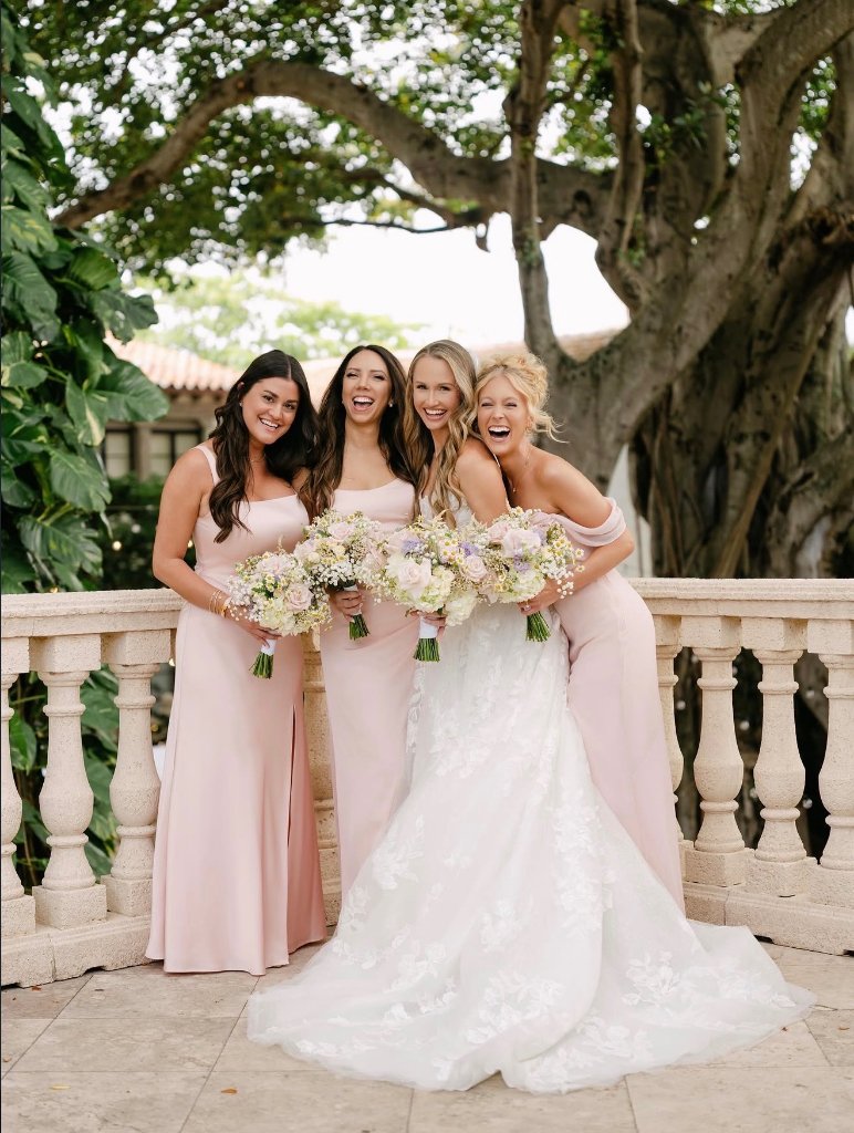 Bride and bridesmaids in blush pink gowns holding bouquets at outdoor wedding venue