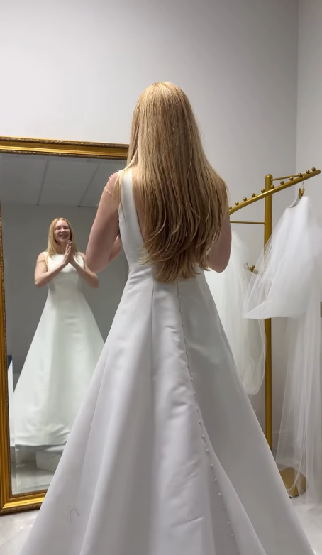 Happy bride smiling at reflection in mirror during wedding dress fitting at Bridal and Couture Alterations boutique Boynton Beach