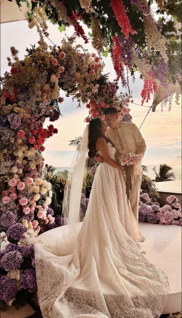 Bride and groom sharing an intimate moment beneath a floral arch at a sunset wedding ceremony