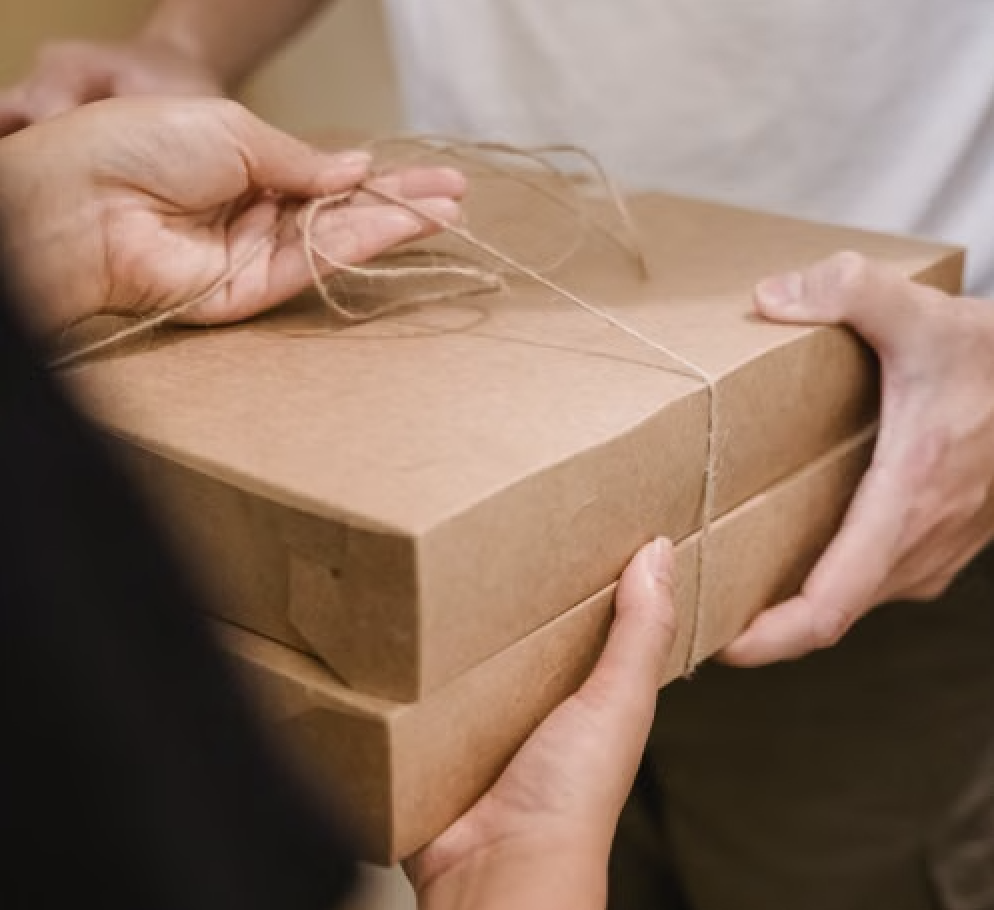 Hands passing over a kraft bakery box tied with twine during a delivery