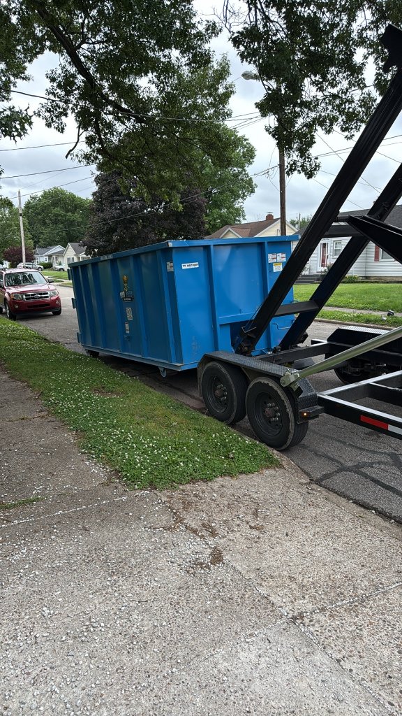 Blue dumpster being loaded onto flatbed truck
