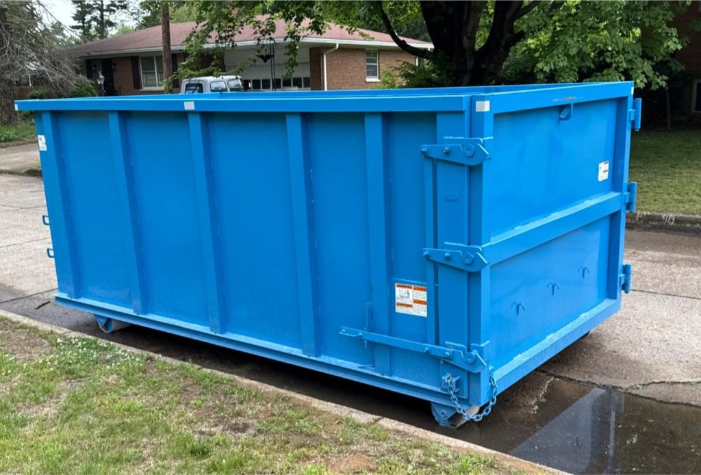 Blue dumpster on paved street with houses