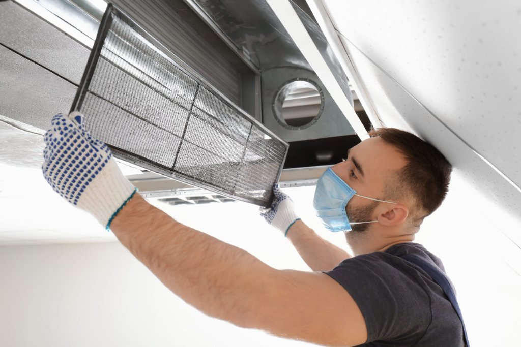 Technician in mask removing an air duct filter for cleaning and sanitizing