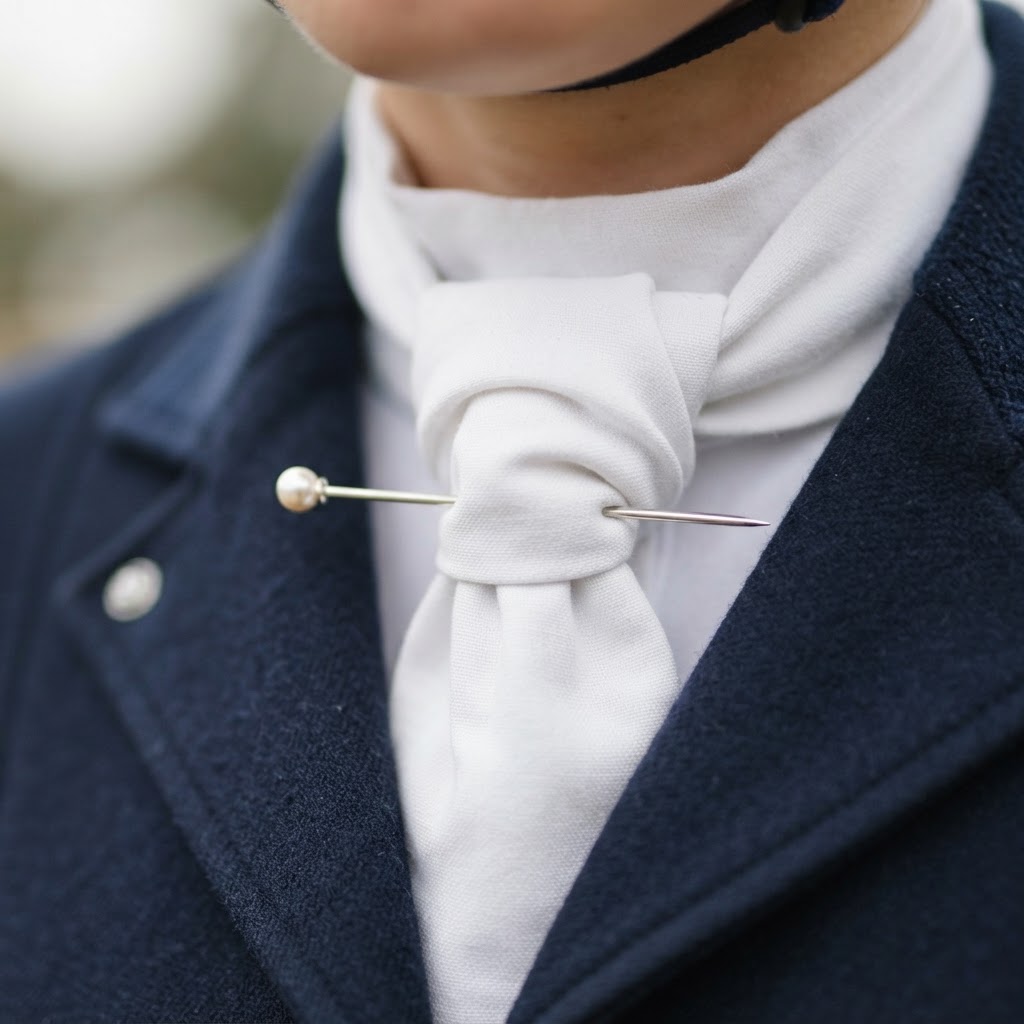 Close-up of a stock pin being inserted horizontally through a white stock tie knot