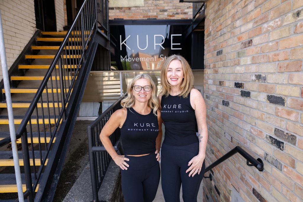 The two founders of KURE MOVEMENT STUDIO standing in front of the studio sign