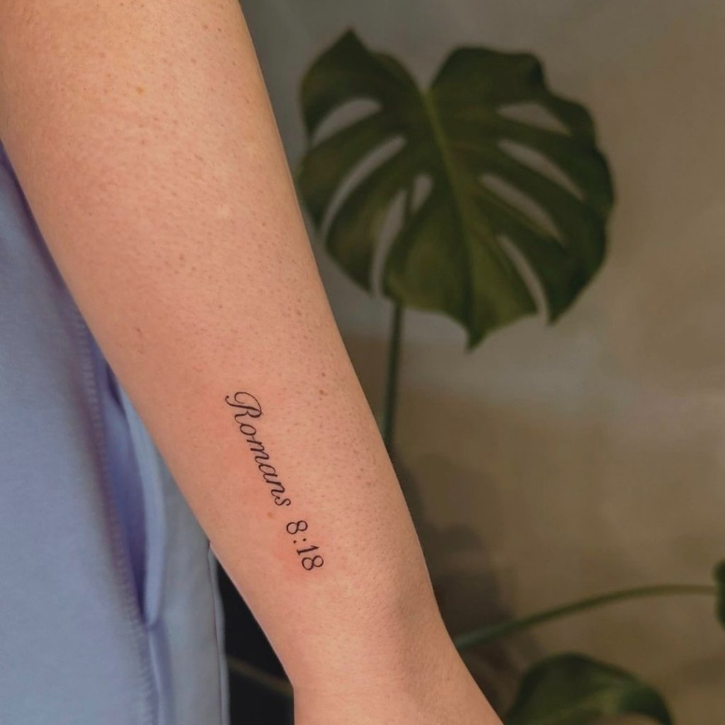 Fine line "Romans 8:18" script tattoo on forearm